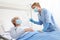 Nurse with thermometer measures fever on elderly woman patient lying in the hospital room bed, wearing protective gloves and