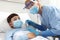 Nurse with thermometer measures fever on patient child in hospital bed, wearing protective visor and surgical mask, corona virus