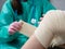 A nurse wearing medical gloves and a mask wraps an elastic bandage around the patient& x27;s leg and knee. Traumatologist