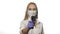 Nurse on white background in mask look directly at camera raises thermometer and measures temperature. She looks at