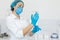 A nurse in a white coat puts on rubber gloves before a medical procedure in a bright handling room