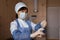 Nurse in a white mask in blue medical clothing stands holding a syringe in her hand.
