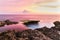 Nusa Lembongan Coast at sunset. Rocky shore, tidepool, Ocean. Water pink from reflection. Pink and yellow sky.