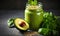 Nutritious green smoothie in glass jar with spinach leaves, half avocado, and chia seeds on grey backdrop - a healthful vegan