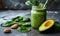 Nutritious green smoothie in glass jar with spinach leaves, half avocado, and chia seeds on grey backdrop - a healthful vegan