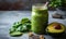 Nutritious green smoothie in glass jar with spinach leaves, half avocado, and chia seeds on grey backdrop - a healthful vegan