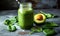 Nutritious green smoothie in glass jar with spinach leaves, half avocado, and chia seeds on grey backdrop - a healthful vegan