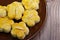 Nyonya almond cookies, piped into flower shapes, on a dark brown saucer, against wooden table