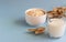 Oat milk in a jug and oats in a white ceramic bowl on a blue paper background.