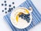 Oatmeal with bananas, blueberries, chia, jam, honey, blue napkin on white wooden background. Healthy breakfast. Top view