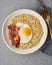 Oatmeal, fried egg and fried bacon. Hearty fat high-calorie breakfast, source of energy. Vertical