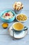 Oatmeal with fruit pieces and candied strawberries, white raisins, apple chips, honey in small bowls and a cup of green tea