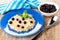 Oatmeal with milk, blueberry, leaves of mint in plate, napkin, bowl with blackcurrant, spoon on wooden table