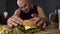 Obese man cooking big burger, overeating gourmet admiring his meal, close-up