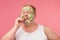 Obese man with cucumber mask on face, eats slice of cucumber, isolated on pink.