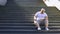 Obese man sitting down on stairs to rest for minute, exhausted after workouts