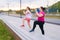 Obese overweight young woman doing single leg squats using bench with personal trainer outdoor in summer morning.