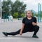 Obese young caucasian woman doing side lunges. Fat beautiful smiling girl in a black tracksuit is engaged in fitness