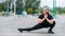 Obese young caucasian woman doing side lunges. Fat beautiful smiling girl in a black tracksuit is engaged in fitness