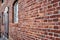 Oblique view of a red old weathered brick wall with a blurred window at the end