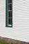 Oblique view of a window in a white painted clapboard church building trimmed in green