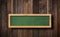 Oblong green blackboard hanging on ropes with wood planks background