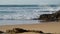 Ocean crashing rocky beach on sunny day. White foamy waves rolling coastline