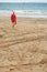 Ocean sand in focus with many foot prints. Lifeguard walking towards a flag in water out of focus