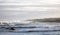 Ocean sunset view with vacation homes in the background and rocks and waves in the foreground.