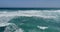 Ocean surf, waves and white sea foam against a light blue sky. Seascape of foamy breaking waves, blue ocean and blue sky