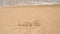 Ocean wave approaching word love written in sand