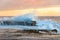 Ocean wave crushing over rock with splashes of white foam at sunrise