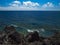 Ocean waves breaking on the rocky coast of hardened lava with caverns and cavities. Deep blue sky with white clouds on the horizon