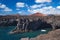 Ocean waves breaking on the rocky coast of hardened lava with caverns and cavities. Deep blue sky with white clouds and mountains