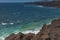 Ocean waves breaking on the rocky coast of hardened lava with caverns and cavities. Mountains and volcanoes on the horizon