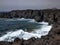 Ocean waves breaking on the rocky coast of hardened lava with caverns and cavities. Mountains and volcanoes on the horizon