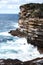 Ocean waves crashing onto jagged rock cliff face