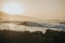 Ocean waves hitting the rocky beach and gleaming under the golden sunrays