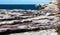 Oceanside rocky cliff top sandstone wave ridges with blue coastal sea and sky in background