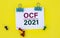 OCF 2021 - acronym on white paper with clips on yellow background with buttons and pencil