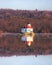 Octagonal wooden lighthouse with a white house and red mansard roof in the middle of a river reflecting in the water.