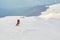 Off piste skier, wearing colorful red clothes, descending on a ridge in Baiului mountains, Romania, towards the foggy forest