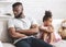 Offended black girl and dad sitting on sofa at home