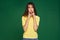 Offended funny young girl touching by fingers puffed cheeks, making faces, teasing, grimacing on green studio background