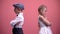 Offended kids couple standing back in silence after quarrel, pink background