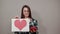 Offended woman in glasses holds a gift, piece of paper with red heart