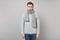 Offended young man in gray sweater, scarf pouting lips on grey wall background, studio portrait. Healthy