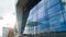 Office building with glass Windows which reflect the floating clouds, along the building there are people. Timelapse