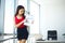 Office. Business Woman Standing at the Grand Window. Light Modern Office. Dressed in Red Sweater and Black Skirt. Trim Folder in H