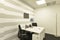 Office cubicle with small white double table with telephones, black swivel chairs, metal coat rack, scratched wall and dark gray